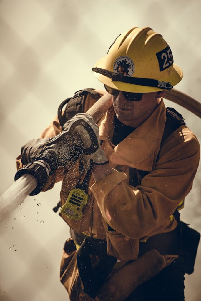 Firefighter equipped with protective gear sprays water during an emergency response.